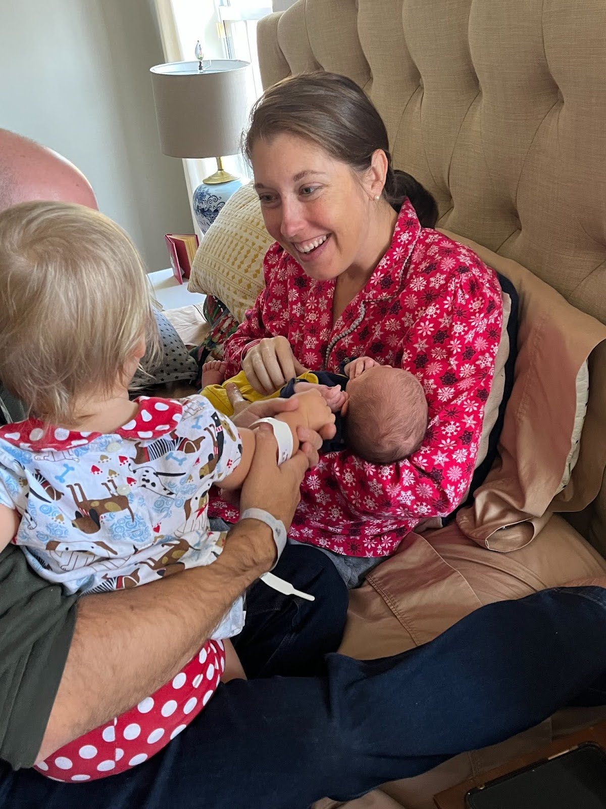 Shelby sitting on a bed, holding her newborn baby while her partner and other child reach out to touch the baby's hand